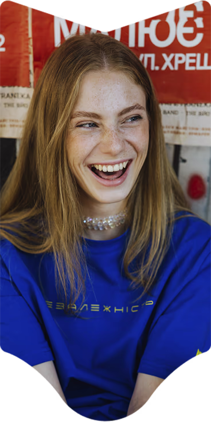 Smiling young woman with long light brown hair wearing a blue shirt and a beaded choker necklace.